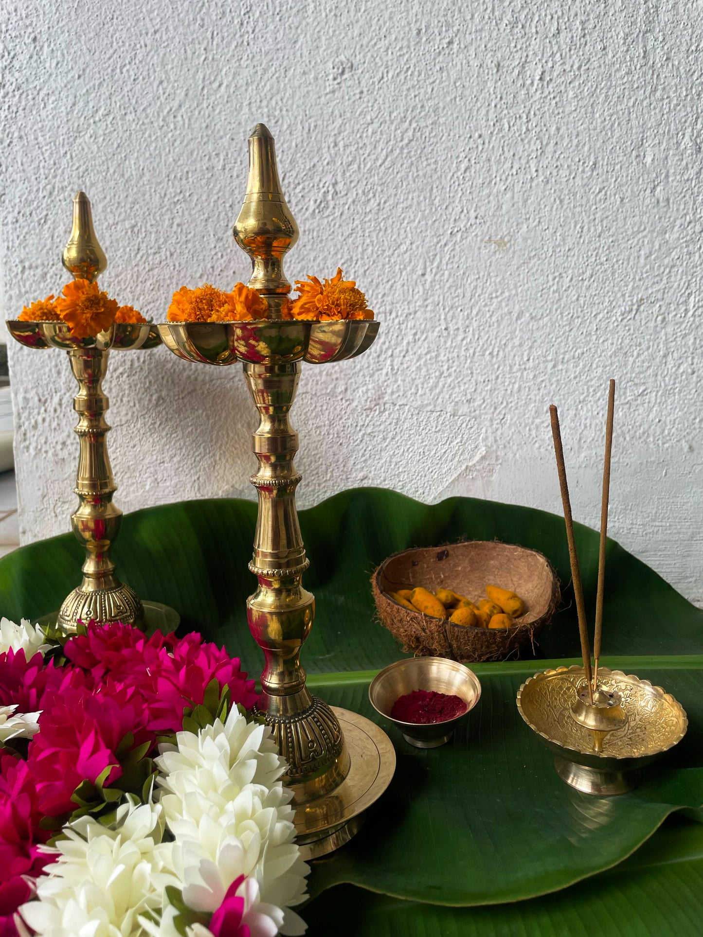 Decorative setup with brass lamps, flowers, and incense on a green leaf