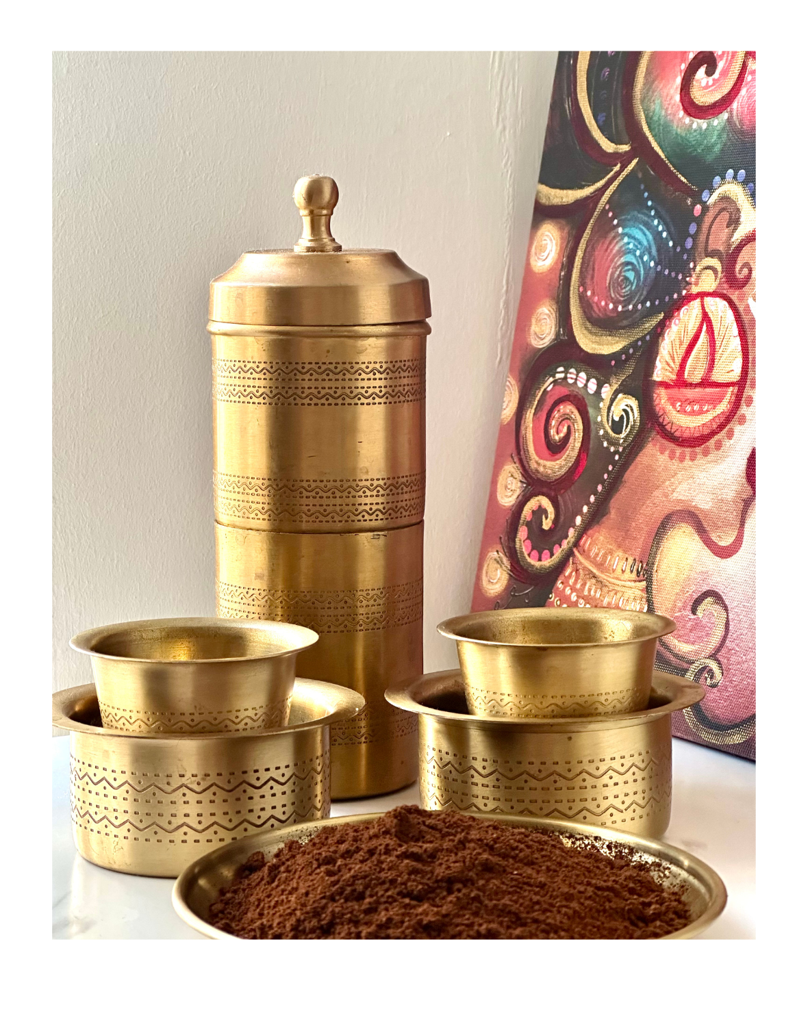 A brass coffee brewing set consisting of a filter, two traditional brass davaras, and a container, displayed alongside coffee grinds.